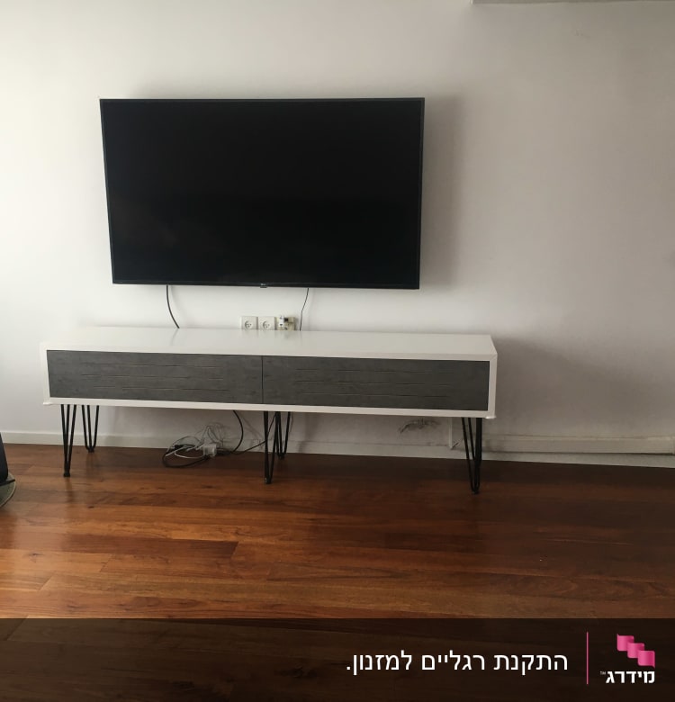 טלוויזיה תלויה על קיר מעל שידה מעץ